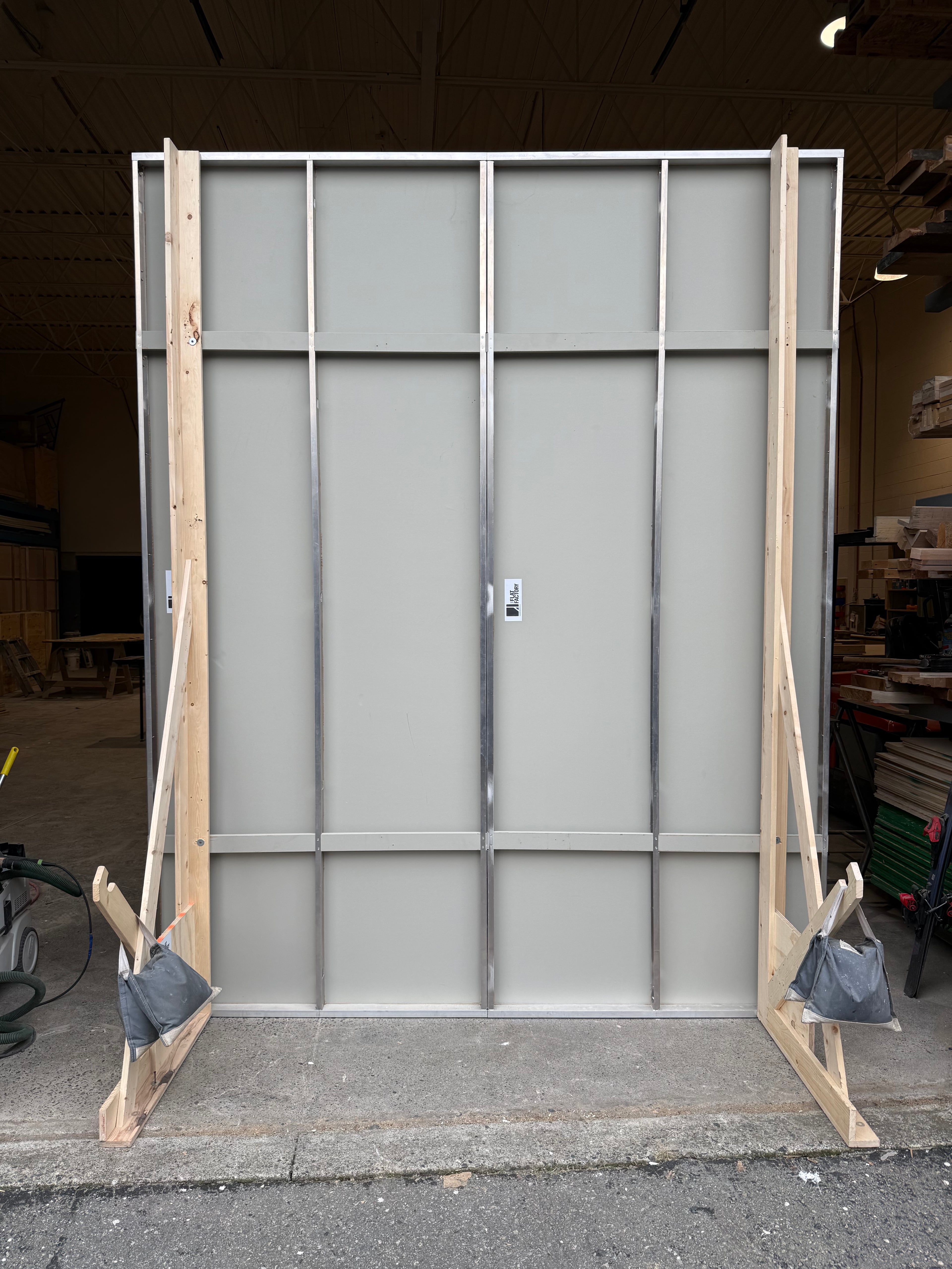 Back view of modular indoor-outdoor wall panel showing metal grid frame and wooden braces in workshop