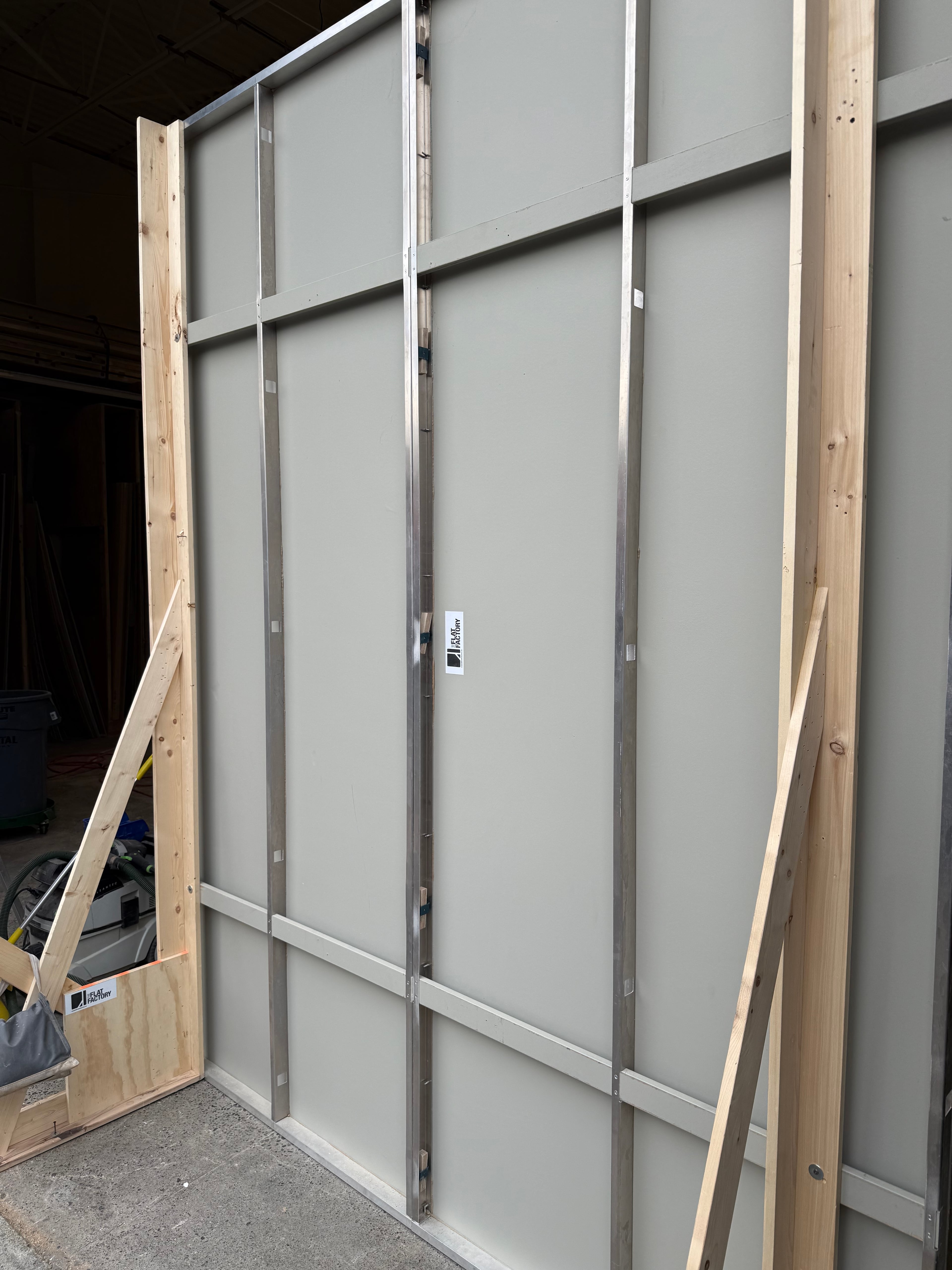 Side view of modular indoor-outdoor wall panel showing metal frame and wooden braces in workshop