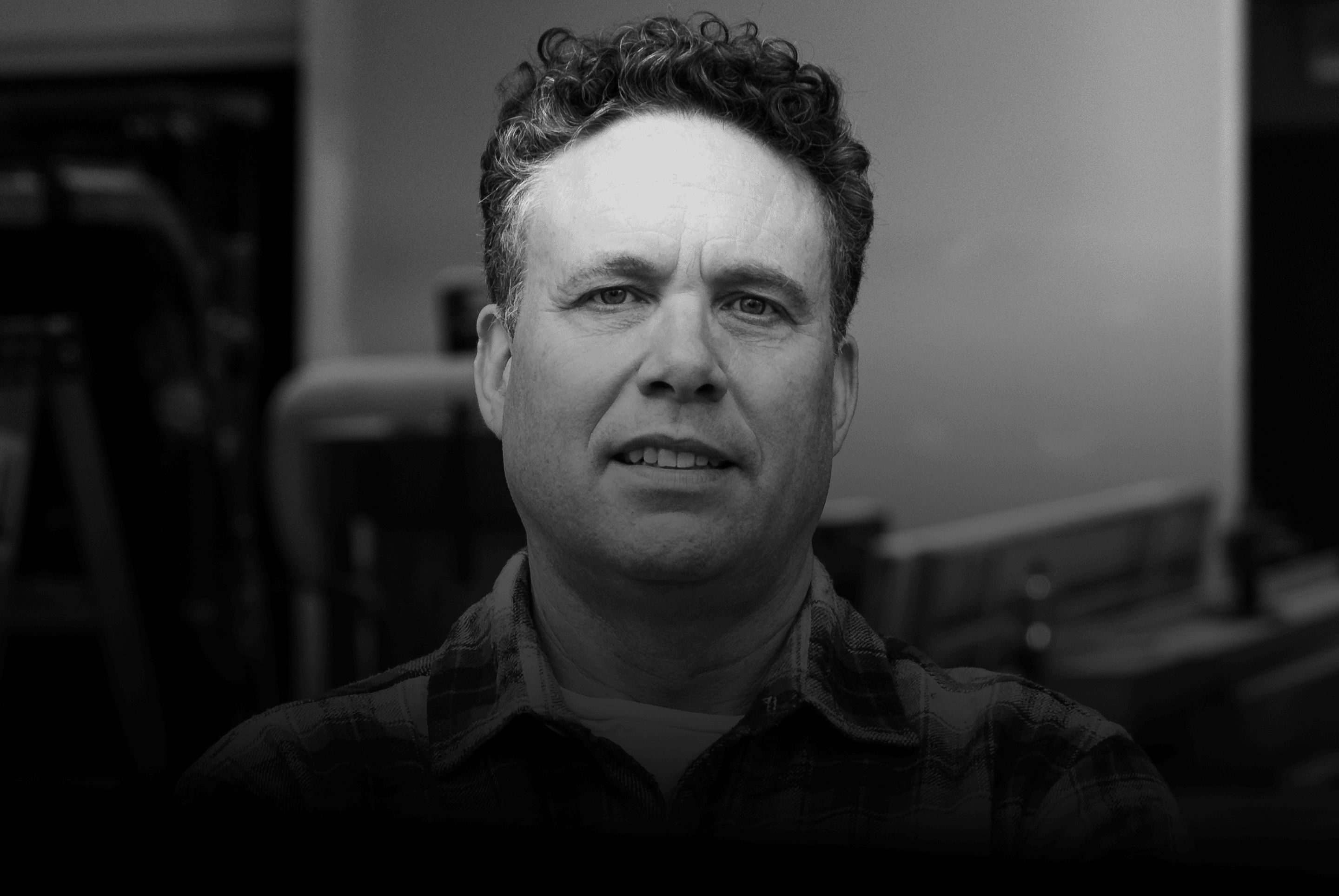 Black and white portrait of Adam Bartlett in a plaid shirt in a workshop setting