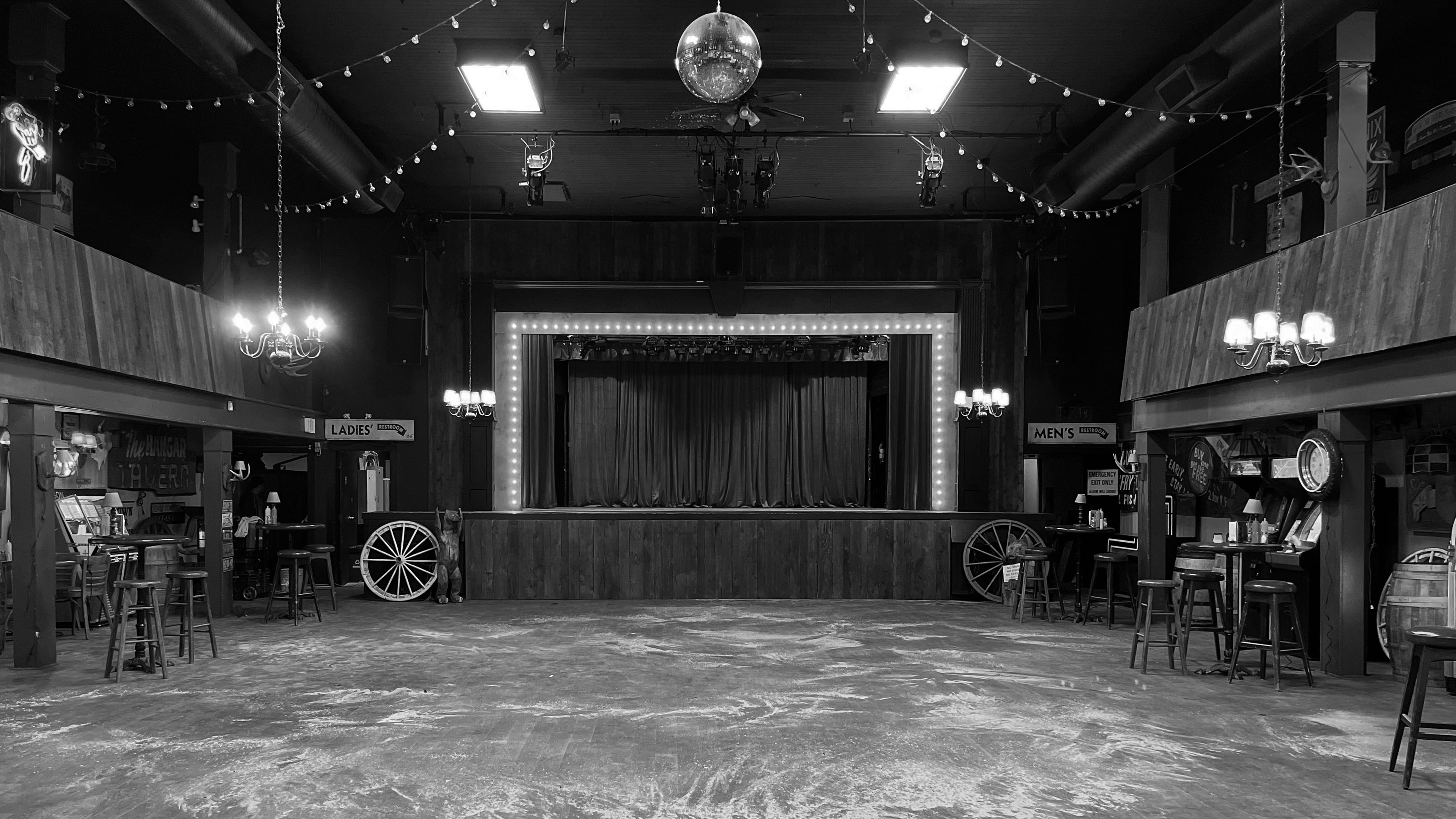 Western honkytonk bar set with red curtain stage, disco ball, wagon wheels, and string lights for Expedia commercial
