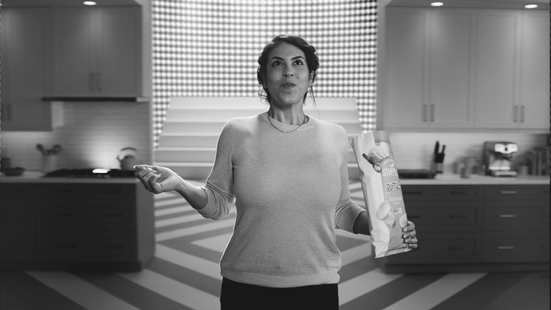 Woman presenting a snack bag in a vibrant blue-lit kitchen set for Frito-Lay commercial