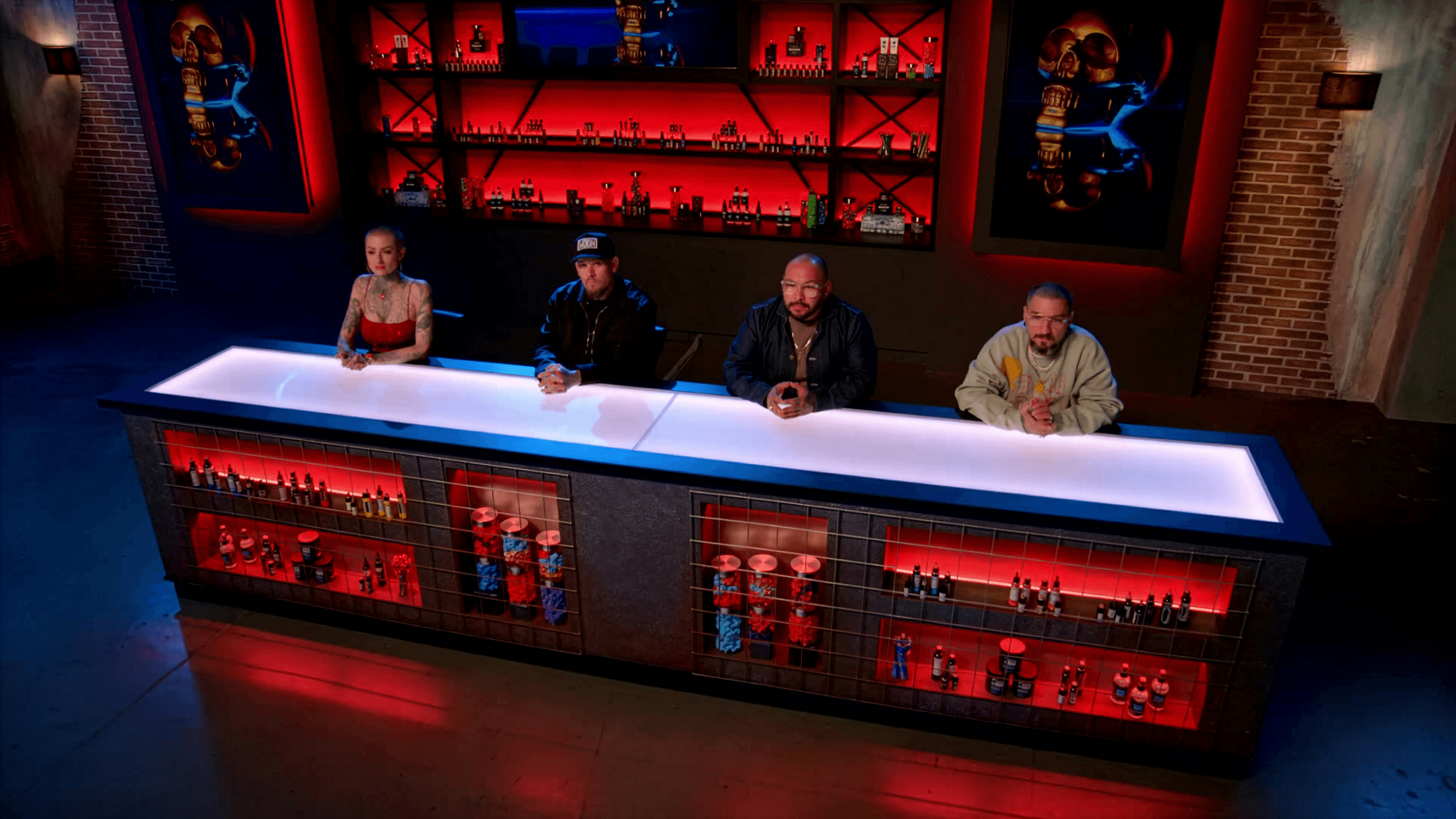 Three judges seated at illuminated desk with red-lit bar backdrop on Ink Master set