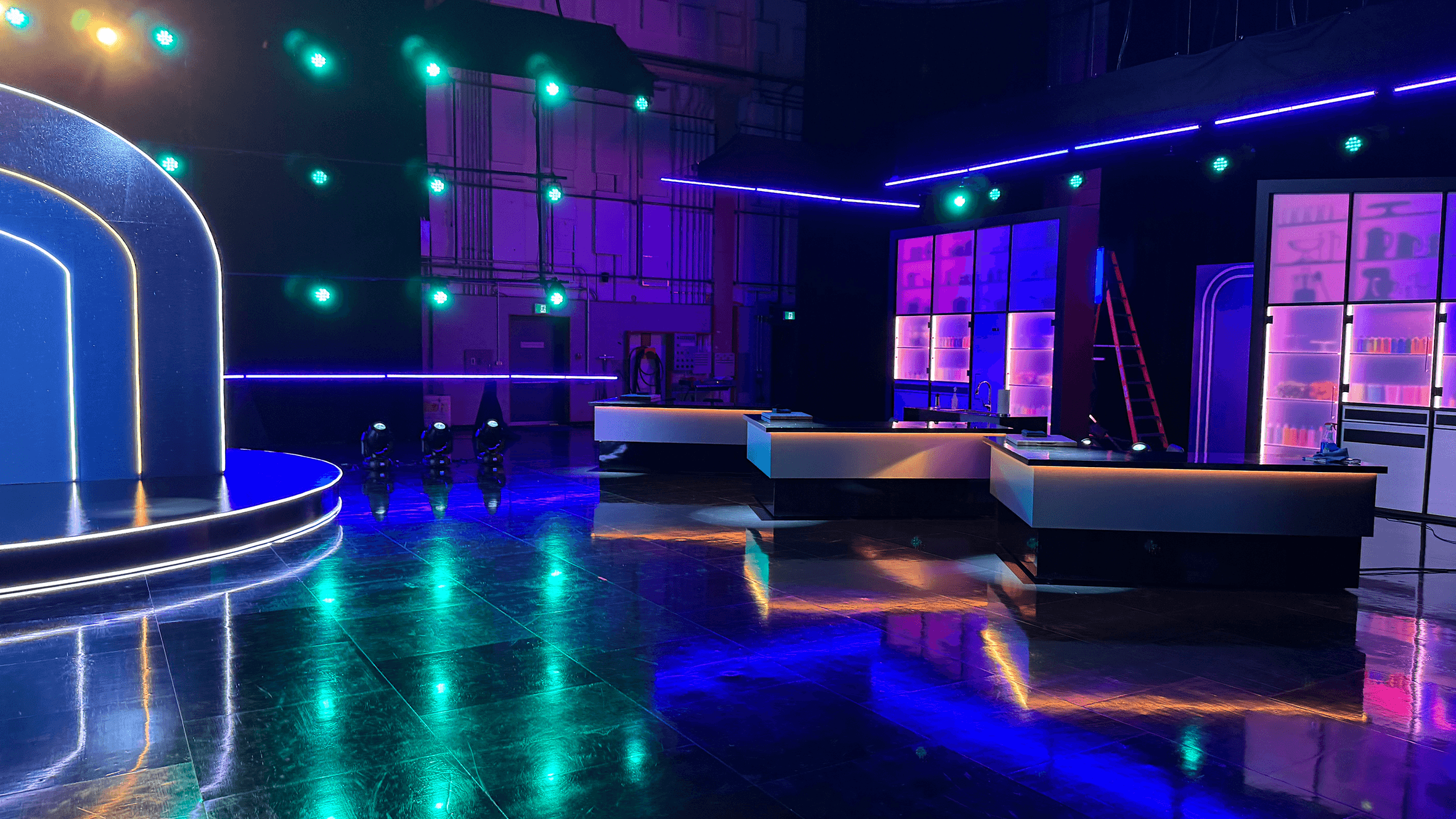 Game show stage set with neon blue and purple lighting, contestant stations, and glossy floor for Is It Cake