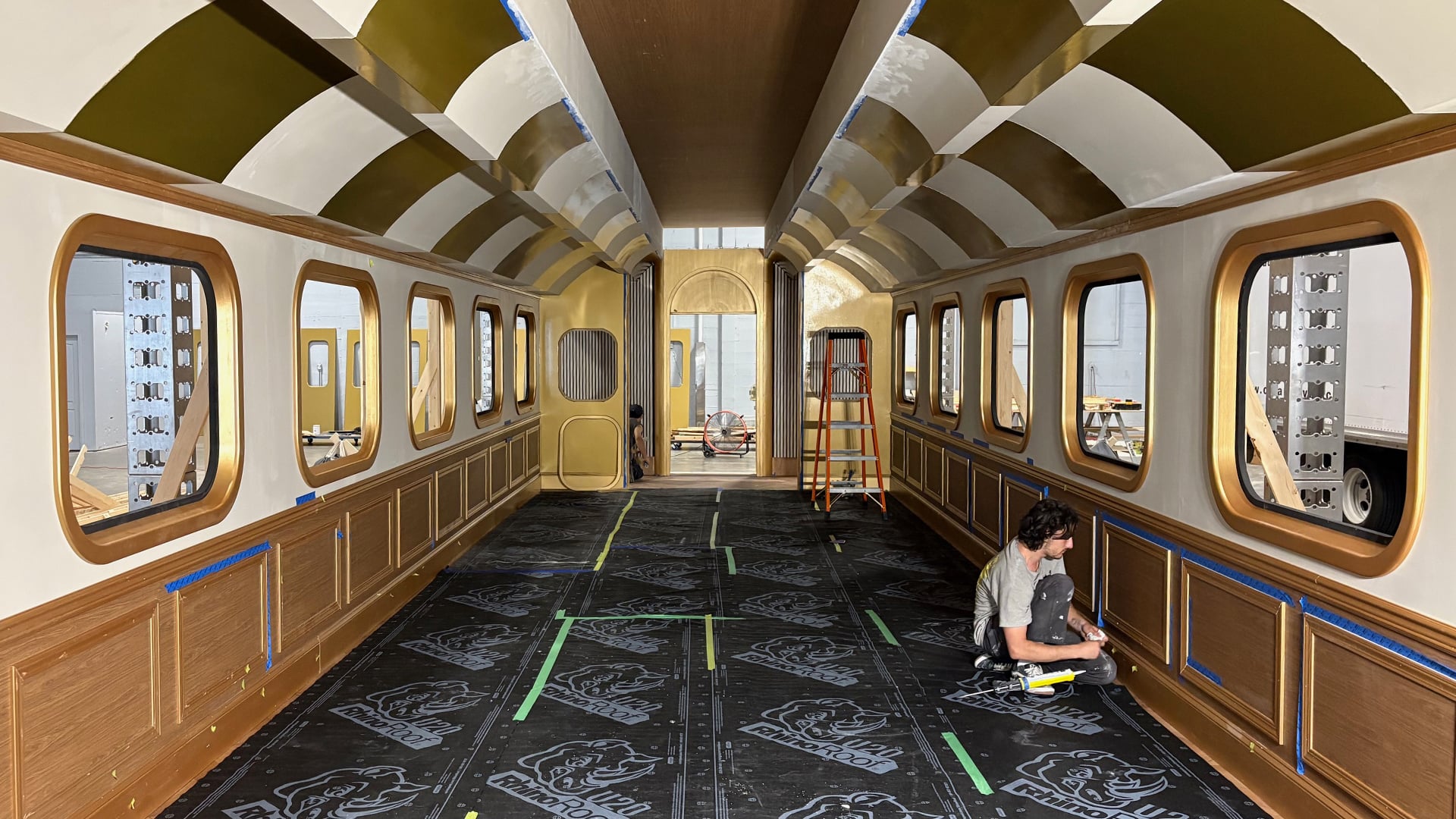 Train cabin aisle interior with arched ceiling, gold wainscoting, and oval windows being finished by crew for MGM Grand