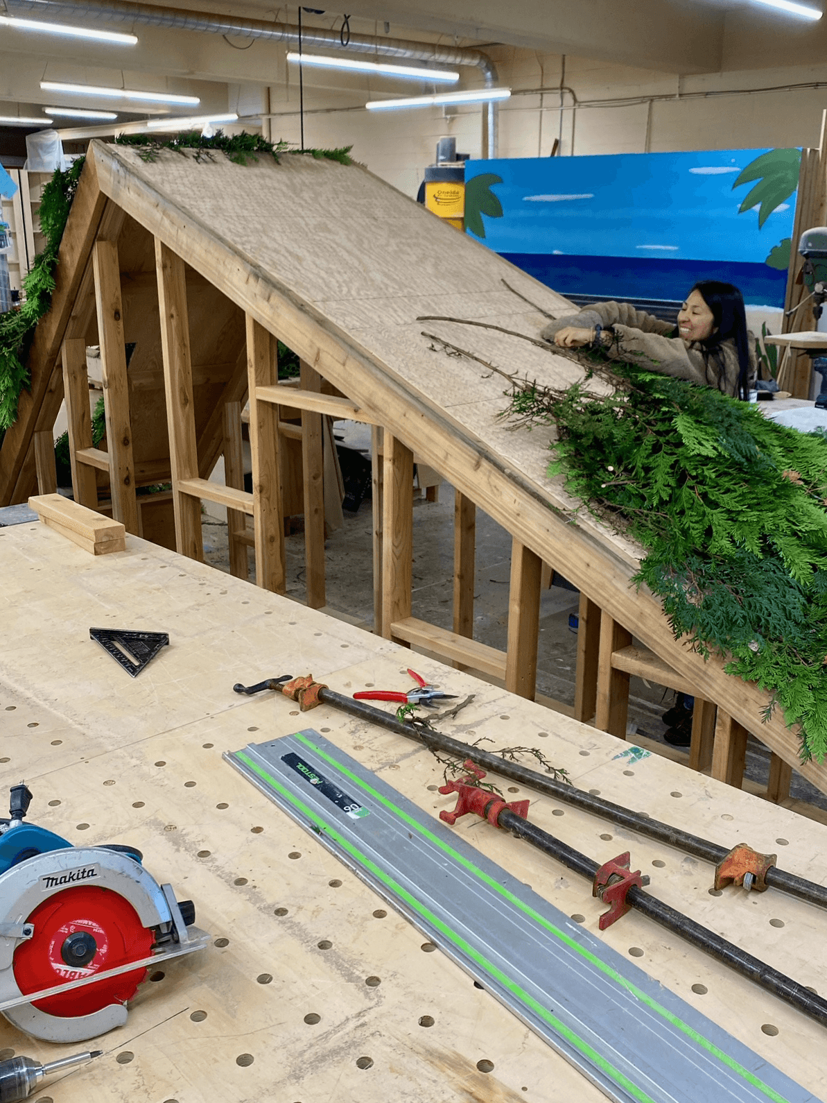 Workshop construction of the Taylor Swift Folklore cabin with crew applying greenery to wooden frame